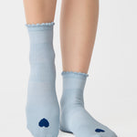 Women wearing a light blue ankle grip sock with a navy blue heart motif on the top made for Pilates, Barre, Yoga, and beyond. 