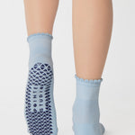 Women wearing a light blue ankle grip sock with a navy blue heart motif on the top made for Pilates, Barre, Yoga, and beyond. 