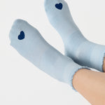 Women wearing a light blue ankle grip sock with a navy blue heart motif on the top made for Pilates, Barre, Yoga, and beyond. 