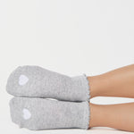 Women wearing a heather grey full foot grip sock with a white heart motif on the top made for Pilates, Barre, Yoga, and beyond. 