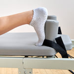 Women on a pilates reformer wearing a heather grey full foot grip sock with a white heart motif on the top made for Pilates, Barre, Yoga, and beyond. 