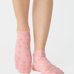 Women wearing a coral pink full foot grip sock with a raised terry heart pattern made for Pilates, Barre, Yoga, and beyond. 