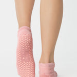 Women wearing a coral pink full foot grip sock with a raised terry heart pattern made for Pilates, Barre, Yoga, and beyond. 