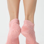 Women wearing a coral pink full foot grip sock with a raised terry heart pattern made for Pilates, Barre, Yoga, and beyond. 