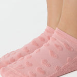 Women wearing a coral pink full foot grip sock with a raised terry heart pattern made for Pilates, Barre, Yoga, and beyond. 