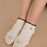 Woman wearing a beige full foot grip sock with a horse on the top and a horseshoe embroidered along the ankle. Made for pilates, barre, and yoga. 