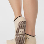 Woman wearing a beige full foot grip sock with a horse on the top and a horseshoe embroidered along the ankle. Made for pilates, barre, and yoga. 