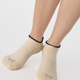 Woman wearing a beige full foot grip sock with a horse on the top and a horseshoe embroidered along the ankle. Made for pilates, barre, and yoga. 