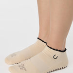 Woman wearing a beige full foot grip sock with a horse on the top and a horseshoe embroidered along the ankle. Made for pilates, barre, and yoga. 