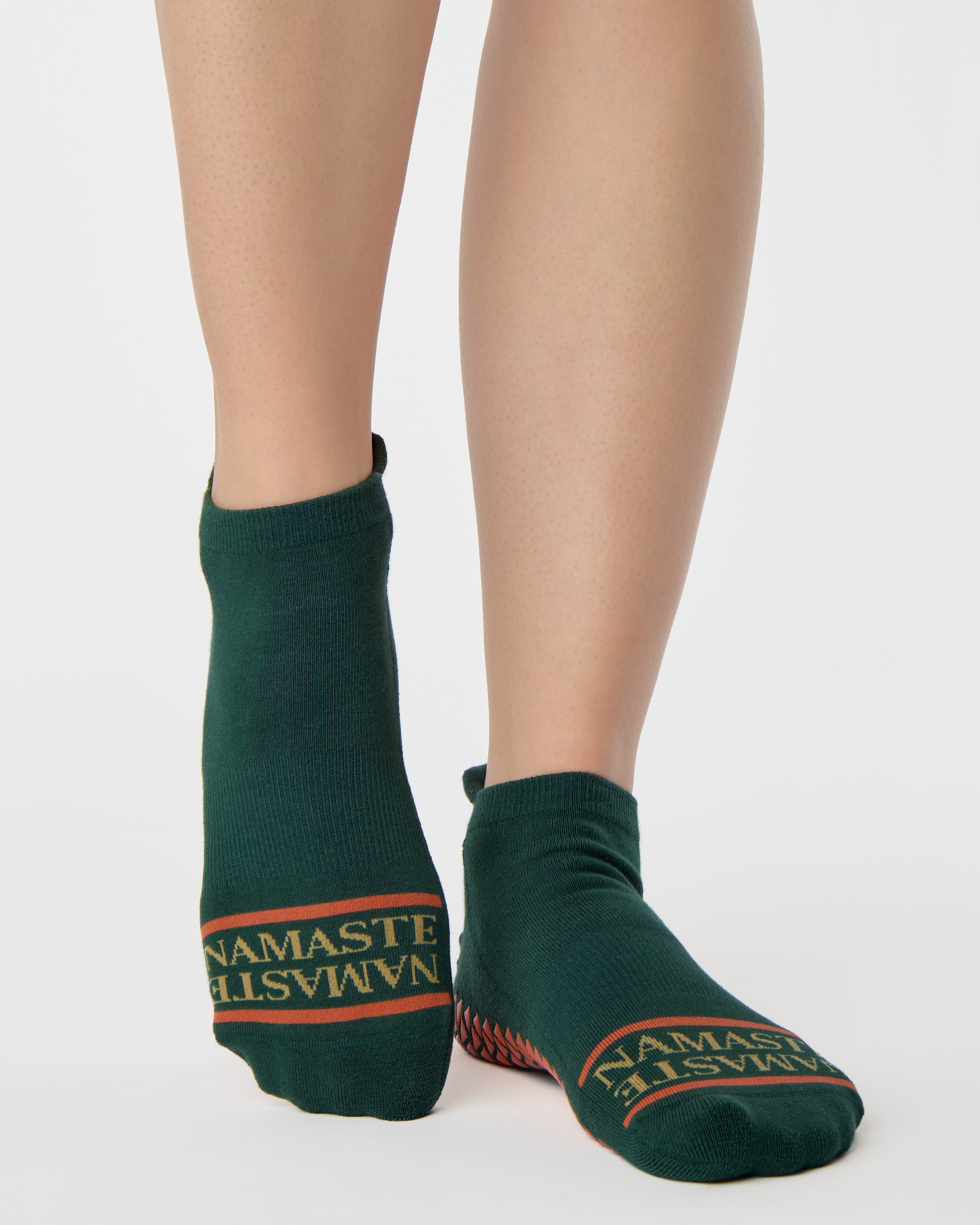 Woman wearing a green full foot grip sock with a yellow namaste message. Made for pilates, barre, yoga, and beyond. 