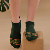 Woman on a yoga block wearing a green full foot grip sock with a yellow namaste message. Made for pilates, barre, yoga, and beyond. 