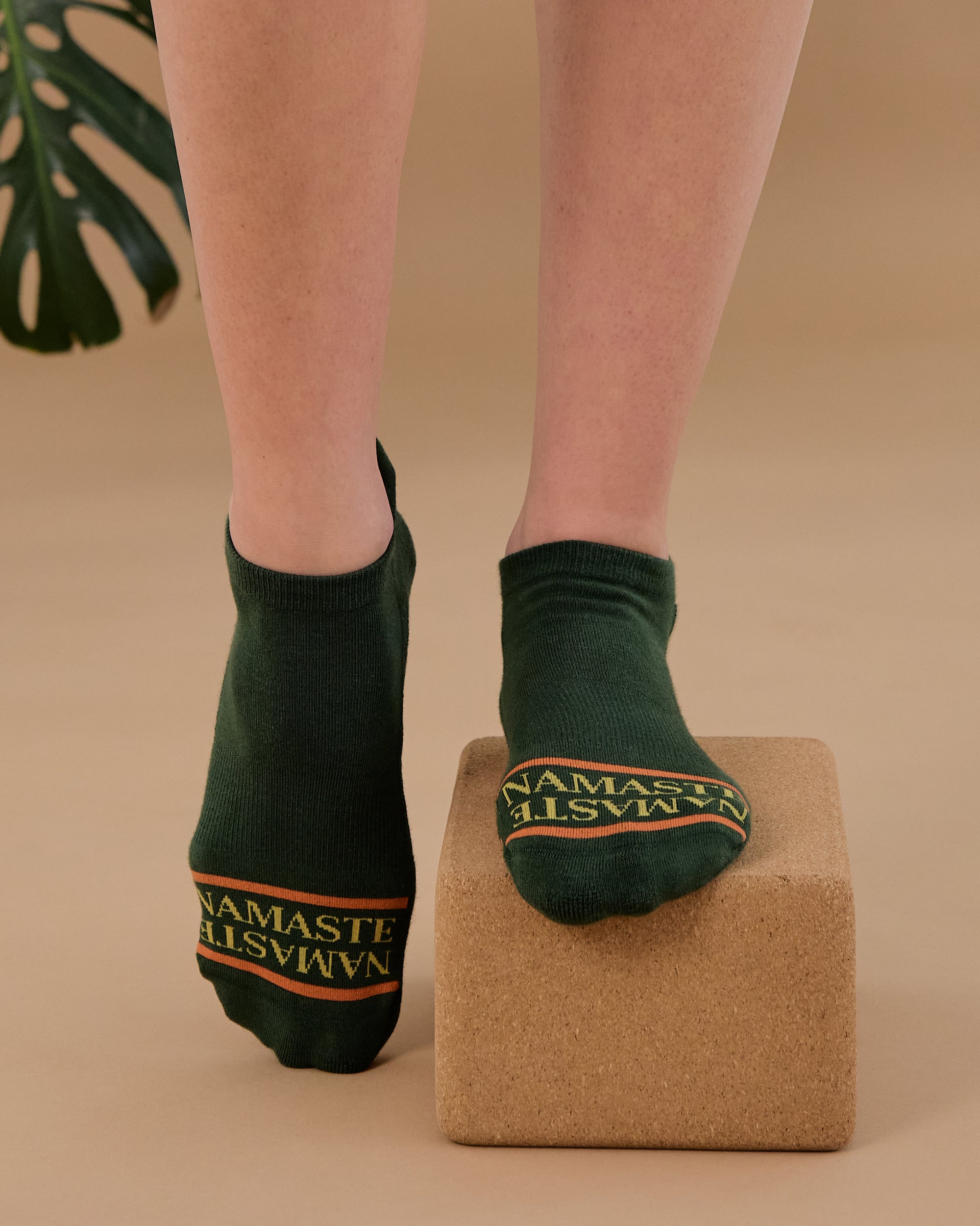 Woman on a yoga block wearing a green full foot grip sock with a yellow namaste message. Made for pilates, barre, yoga, and beyond. 