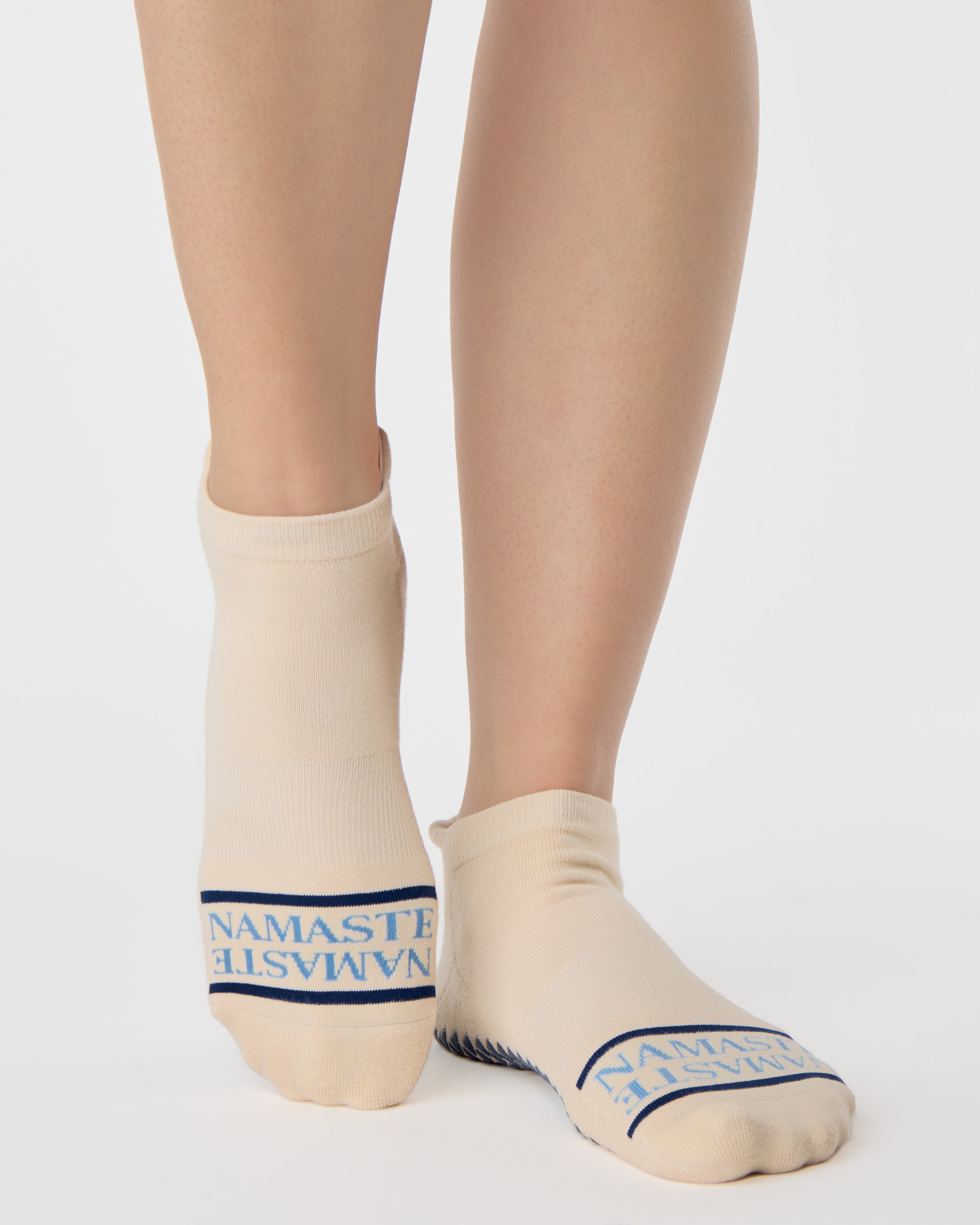 Woman wearing a beige full foot grip sock with a blue namaste message. Made for pilates, barre, yoga, and beyond. 