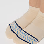 Woman wearing a beige full foot grip sock with a blue namaste message. Made for pilates, barre, yoga, and beyond. 