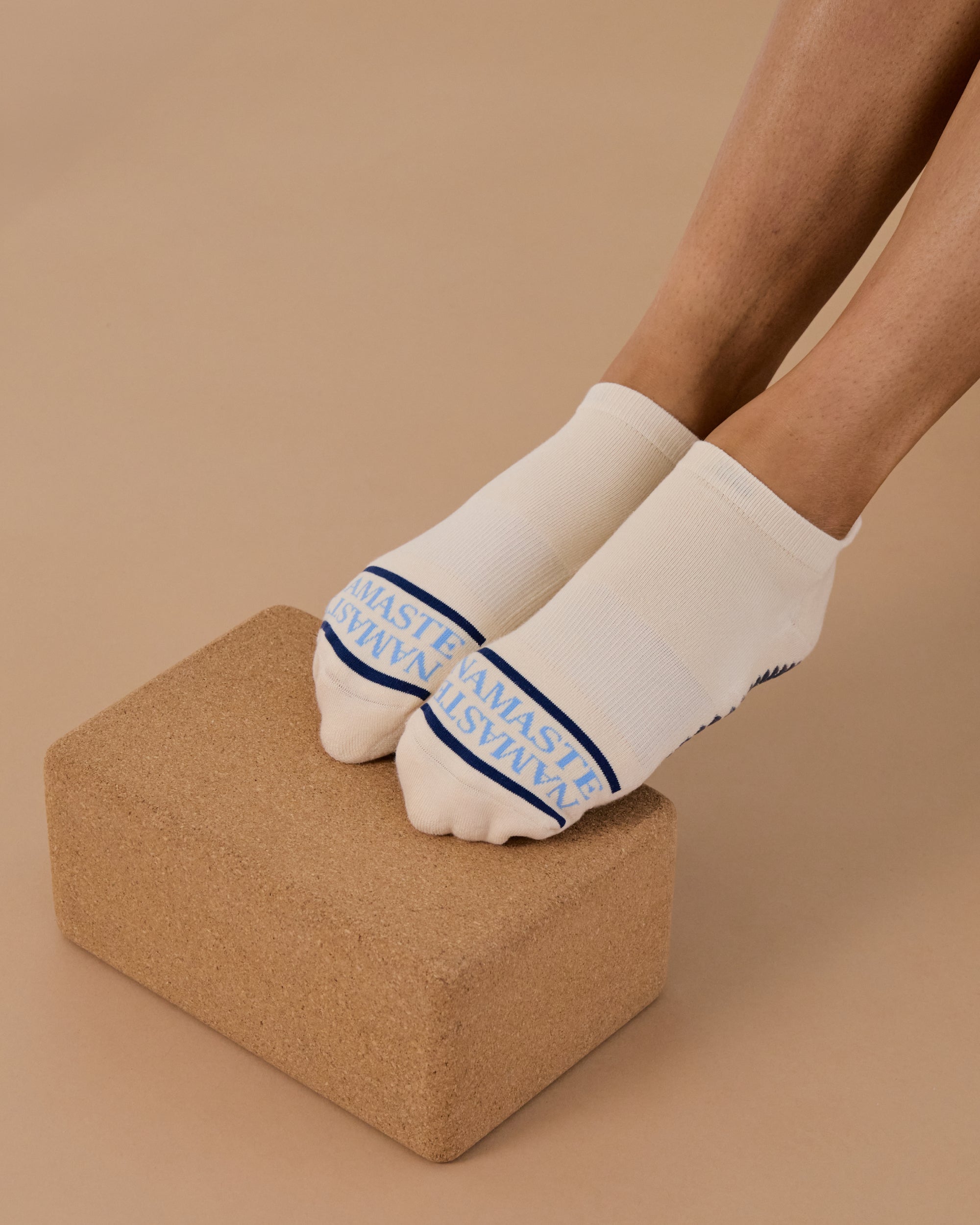 Woman wearing a beige full foot grip sock with a blue namaste message. Made for pilates, barre, yoga, and beyond. 
