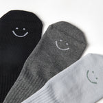 A grip sock pack of mini grip socks for kids ages 4-7, each pair has a happy face motif, black, charcoal and light blue styles.