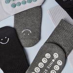 A grip sock pack of mini grip socks for kids ages 4-7, each pair has a happy face motif, black, charcoal and light blue styles.
