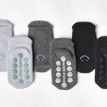 A grip sock pack of mini grip socks for kids ages 1-3, each pair has a happy face motif, black, charcoal and light blue styles.