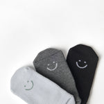 A grip sock pack of mini grip socks for kids ages 1-3, each pair has a happy face motif, black, charcoal and light blue styles.