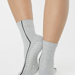 Woman wearing a heather grey solid color ankle grip sock with two black and white bold racing stripes on the side, made for pilates, barre, yoga, and beyond. 