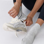 Woman wearing a heather grey solid color ankle grip sock with two black and white bold racing stripes on the side, made for pilates, barre, yoga, and beyond. 