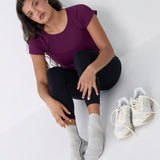 Woman wearing a heather grey solid color ankle grip sock with two black and white bold racing stripes on the side, made for pilates, barre, yoga, and beyond. 