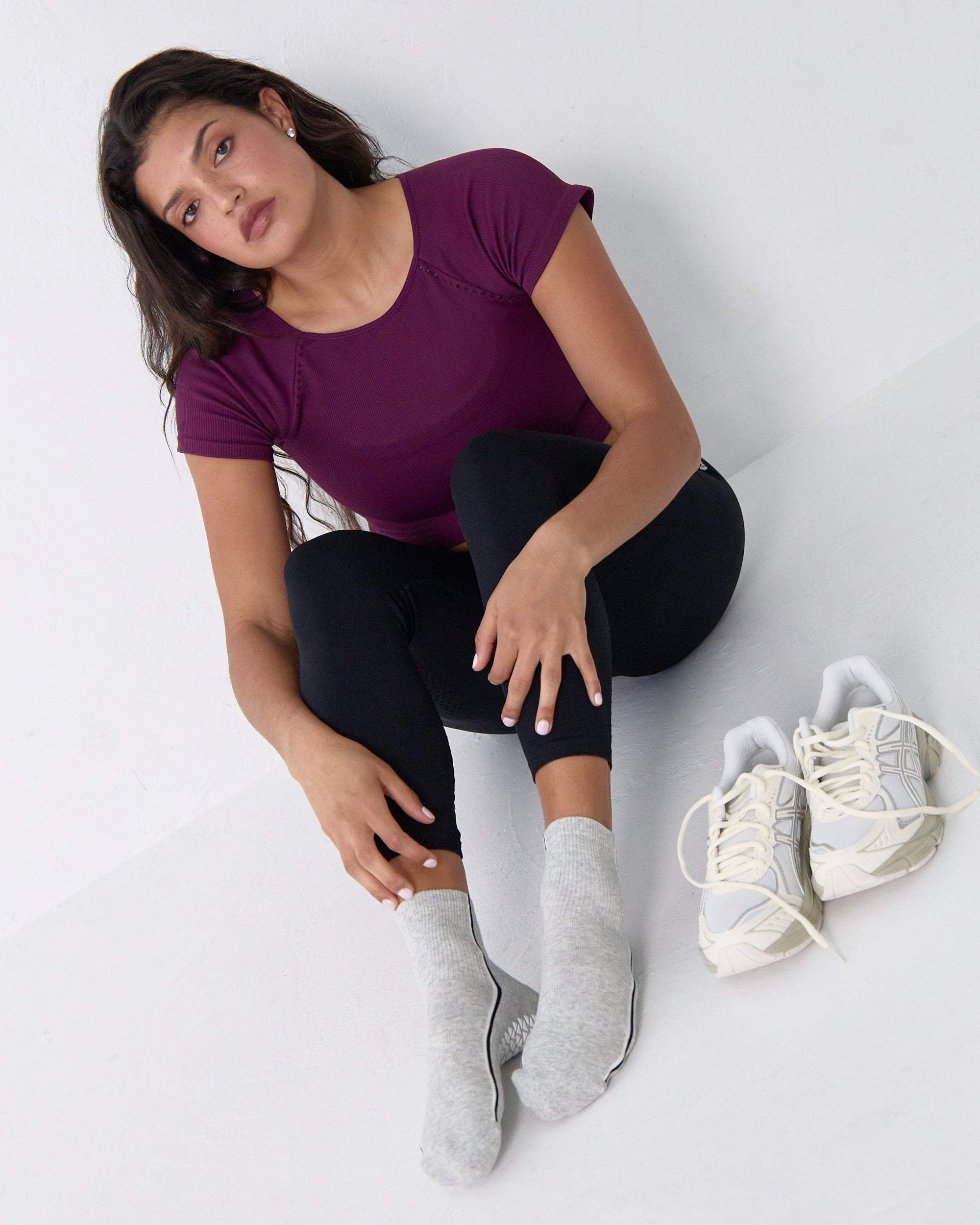 Woman wearing a heather grey solid color ankle grip sock with two black and white bold racing stripes on the side, made for pilates, barre, yoga, and beyond. 