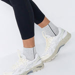 Woman wearing a heather grey solid color ankle grip sock with two black and white bold racing stripes on the side, made for pilates, barre, yoga, and beyond. 