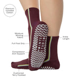 Woman wearing a brownish cherry red solid color ankle grip sock with two green and blue bold racing stripes on the side, made for pilates, barre, yoga, and beyond. With all the product features listed.