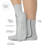 Woman wearing a heather grey solid color ankle grip sock with two black and white bold racing stripes on the side, made for pilates, barre, yoga, and beyond. With all the product features listed. 