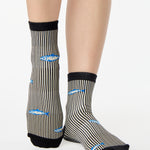 Woman wearing a black and white striped ankle grip sock with sardines swimming around the sock. Made for pilates, barre, yoga, and beyond. 