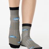 Woman wearing a black and white striped ankle grip sock with sardines swimming around the sock. Made for pilates, barre, yoga, and beyond. 