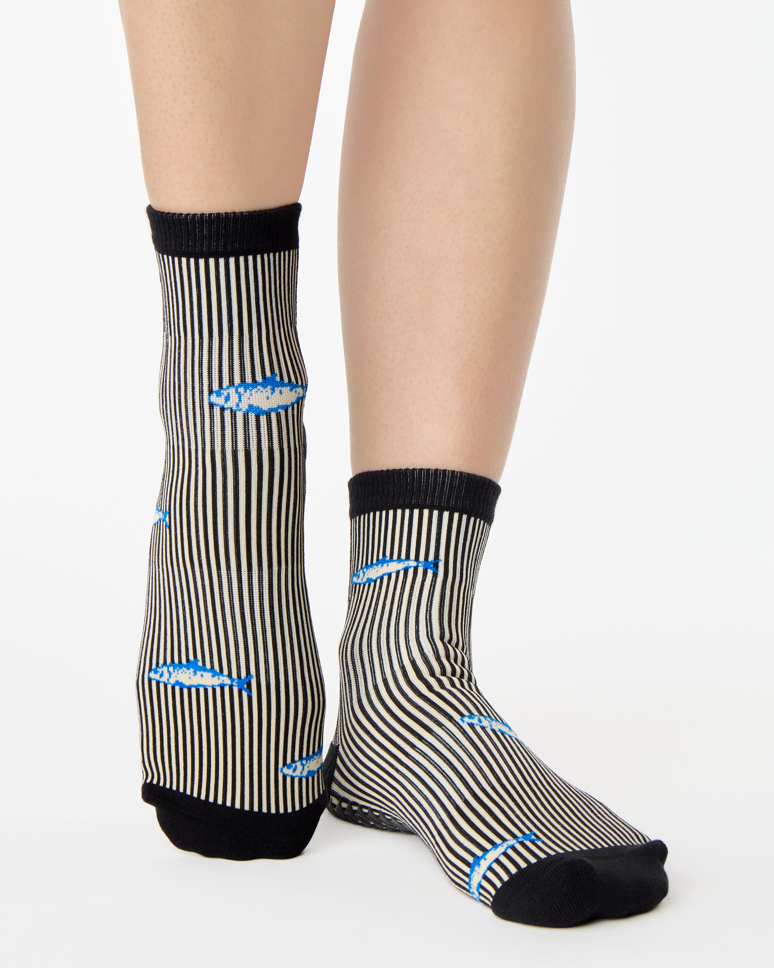 Woman wearing a black and white striped ankle grip sock with sardines swimming around the sock. Made for pilates, barre, yoga, and beyond. 