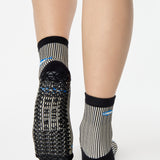 Woman wearing a black and white striped ankle grip sock with sardines swimming around the sock. Made for pilates, barre, yoga, and beyond. 