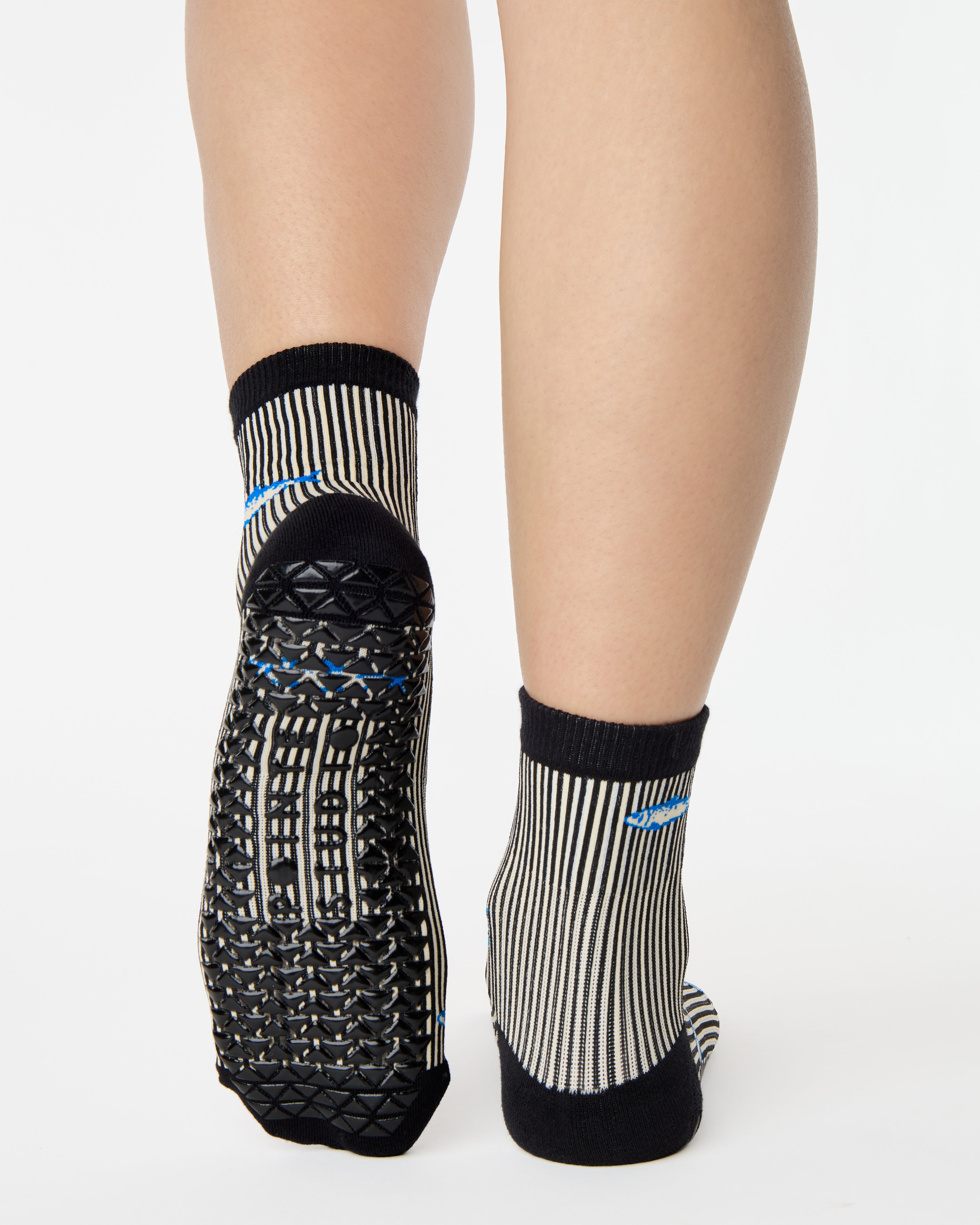 Woman wearing a black and white striped ankle grip sock with sardines swimming around the sock. Made for pilates, barre, yoga, and beyond. 