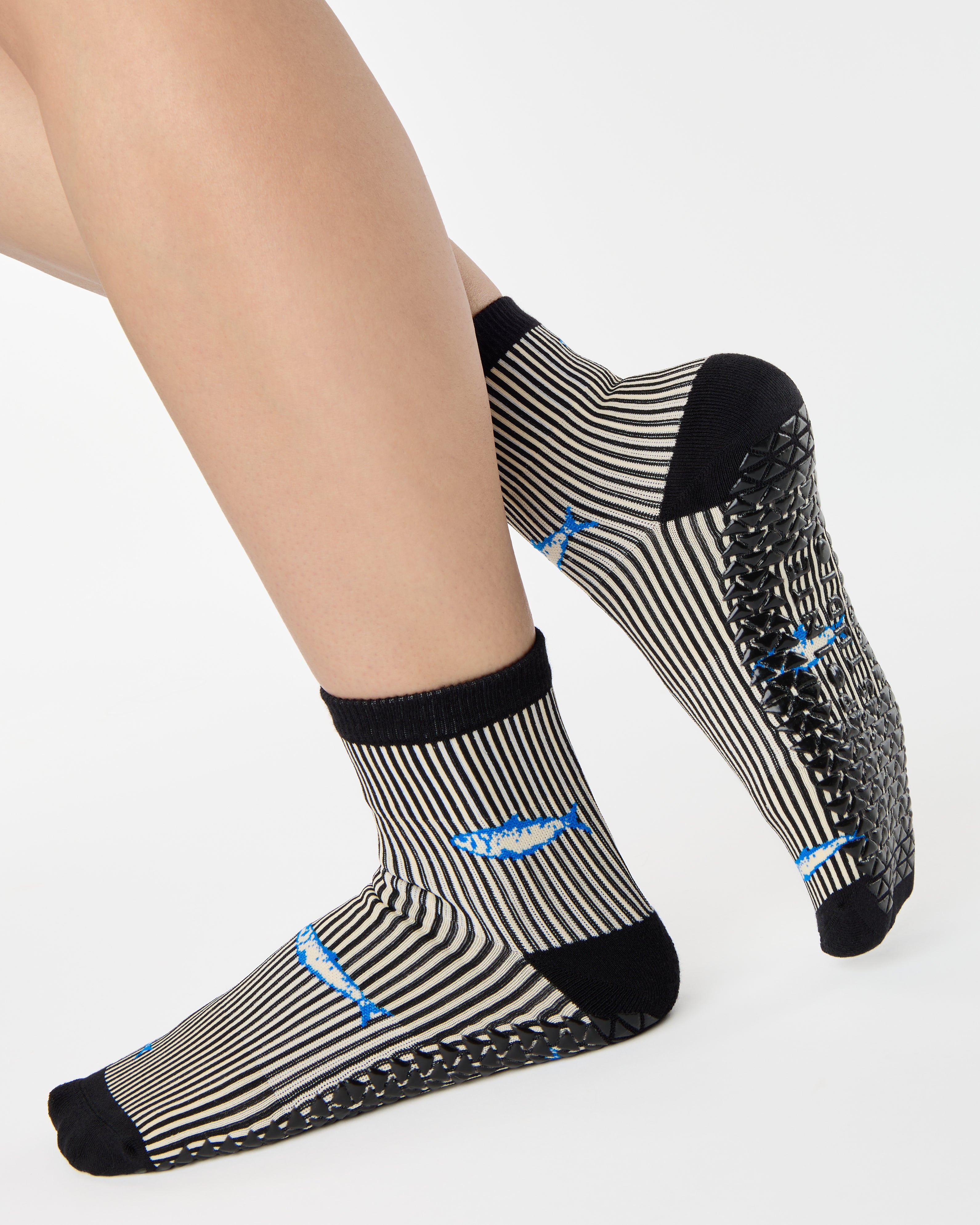 Woman wearing a black and white striped ankle grip sock with sardines swimming around the sock. Made for pilates, barre, yoga, and beyond. 