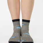 Woman wearing a black and white striped ankle grip sock with sardines swimming around the sock. Made for pilates, barre, yoga, and beyond. 