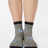 Woman wearing a black and white striped ankle grip sock with sardines swimming around the sock. Made for pilates, barre, yoga, and beyond. 