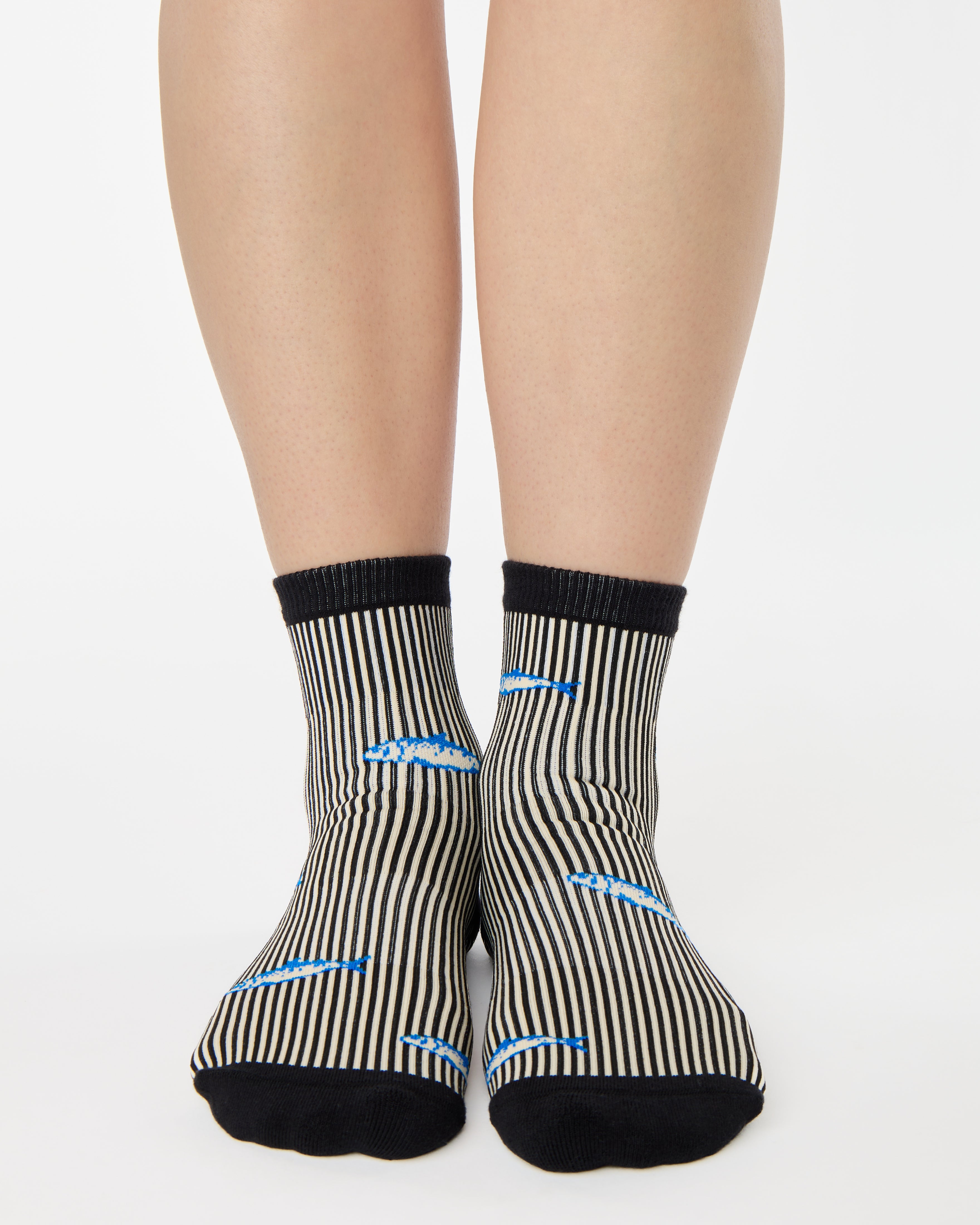 Woman wearing a black and white striped ankle grip sock with sardines swimming around the sock. Made for pilates, barre, yoga, and beyond. 