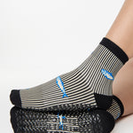 Woman wearing a black and white striped ankle grip sock with sardines swimming around the sock. Made for pilates, barre, yoga, and beyond. 