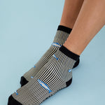 Woman wearing a black and white striped ankle grip sock with sardines swimming around the sock. Made for pilates, barre, yoga, and beyond. 