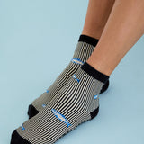 Woman wearing a black and white striped ankle grip sock with sardines swimming around the sock. Made for pilates, barre, yoga, and beyond. 