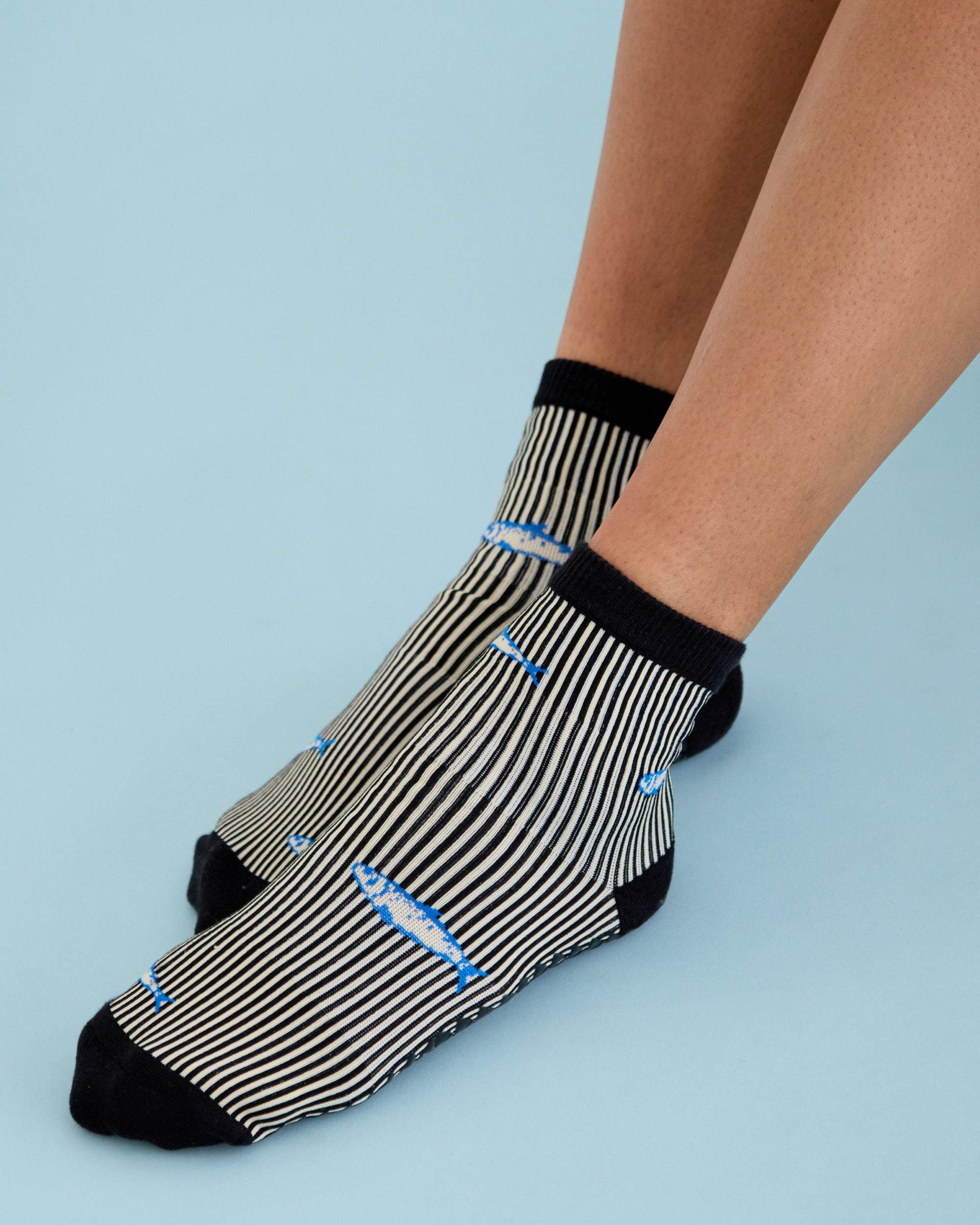 Woman wearing a black and white striped ankle grip sock with sardines swimming around the sock. Made for pilates, barre, yoga, and beyond. 