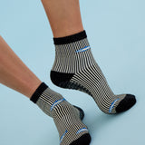 Woman wearing a black and white striped ankle grip sock with sardines swimming around the sock. Made for pilates, barre, yoga, and beyond. 
