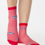 Woman wearing a red and white striped ankle grip sock with sardines swimming around the sock. Made for pilates, barre, yoga, and beyond. 