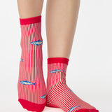 Woman wearing a red and white striped ankle grip sock with sardines swimming around the sock. Made for pilates, barre, yoga, and beyond. 