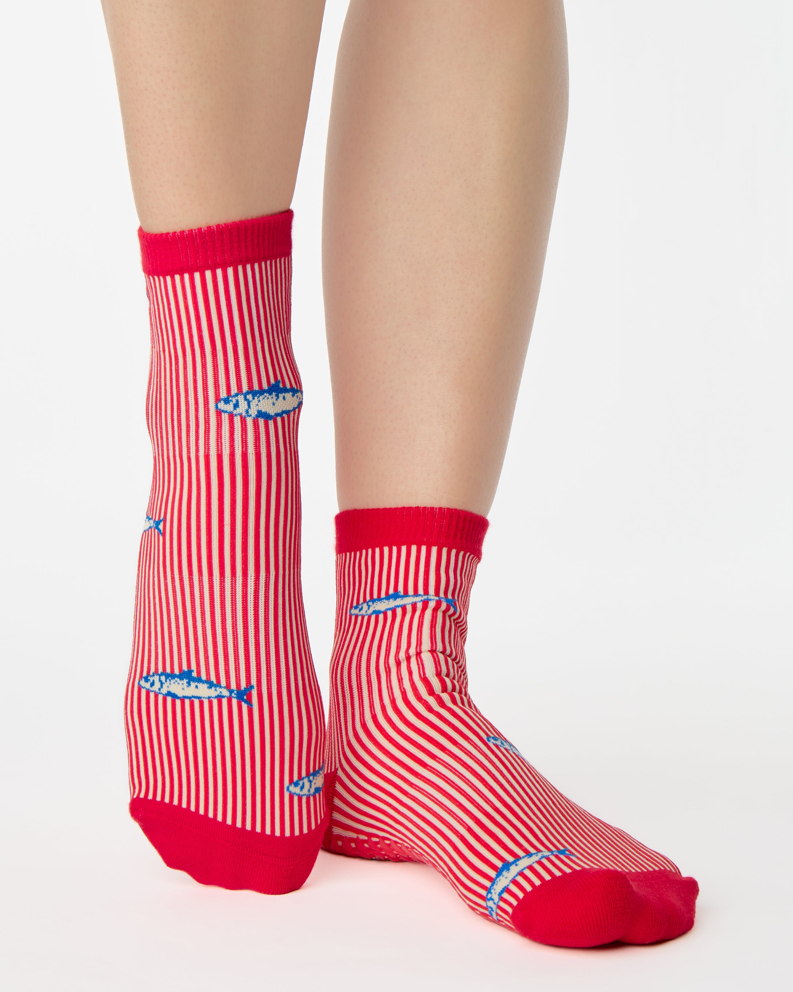 Woman wearing a red and white striped ankle grip sock with sardines swimming around the sock. Made for pilates, barre, yoga, and beyond. 
