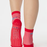 Woman wearing a red and white striped ankle grip sock with sardines swimming around the sock. Made for pilates, barre, yoga, and beyond. 