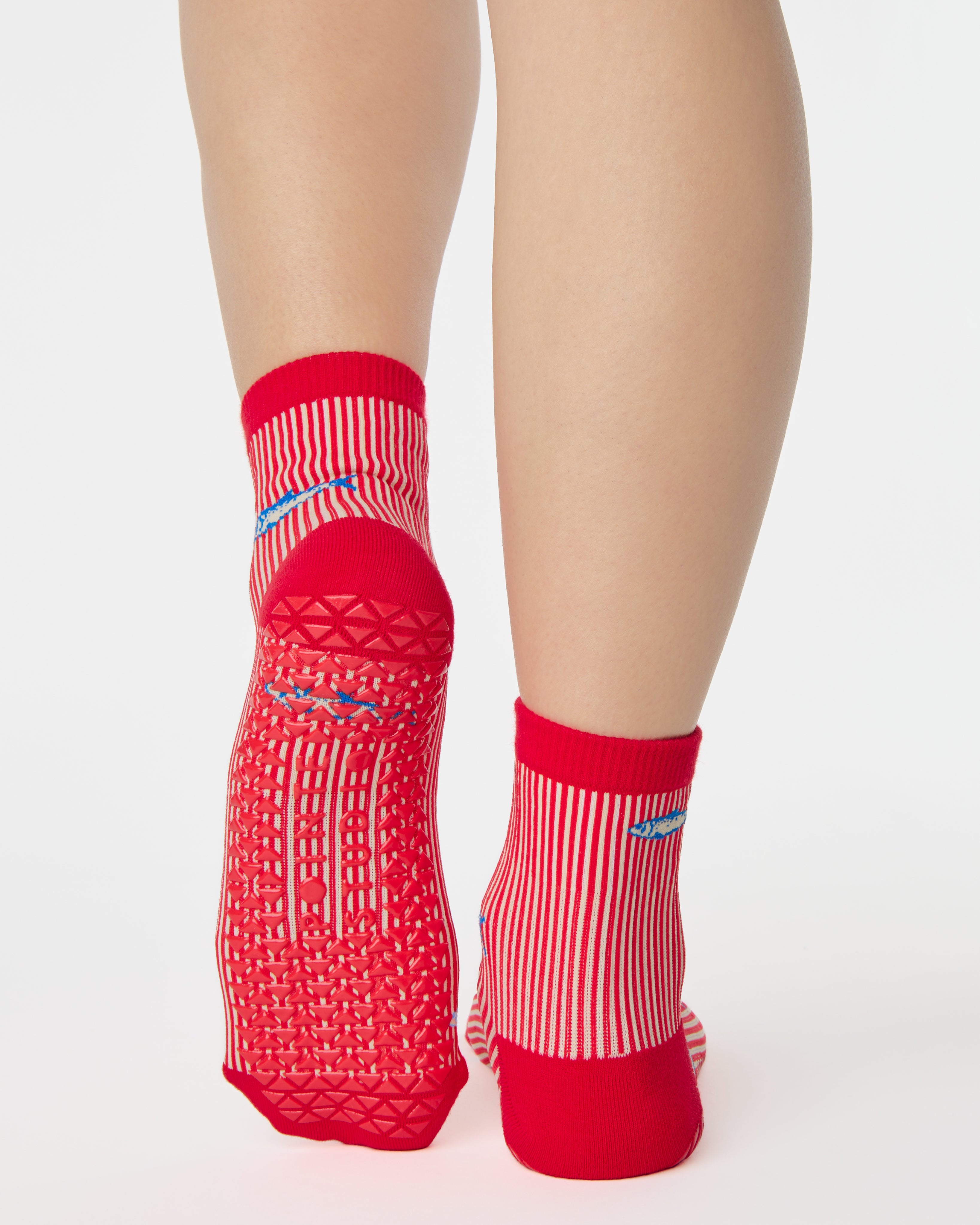 Woman wearing a red and white striped ankle grip sock with sardines swimming around the sock. Made for pilates, barre, yoga, and beyond. 