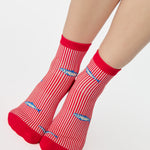 Woman wearing a red and white striped ankle grip sock with sardines swimming around the sock. Made for pilates, barre, yoga, and beyond. 